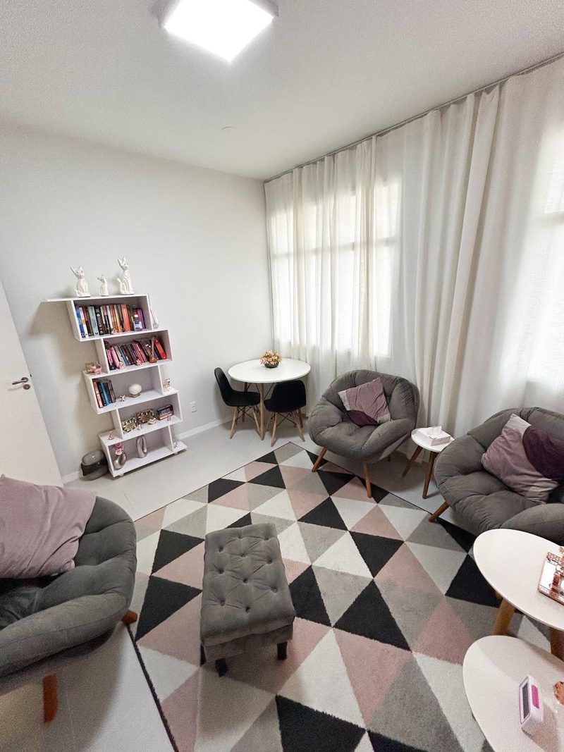Sala de atendimento com poltronas, tapete geométrico e estante de livros